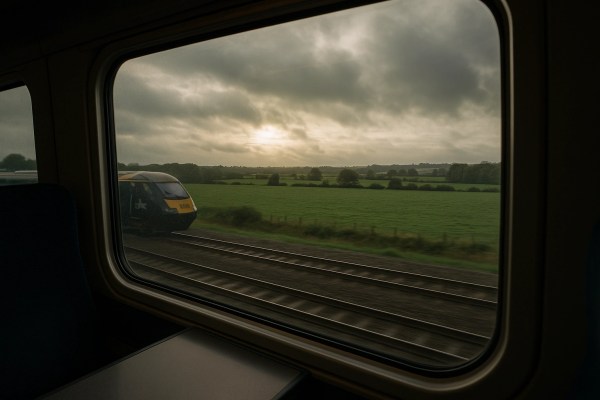 Train ride from London Paddington to Cardiff Central, view through the window showing the Great Western Railway and rolling countryside under a cloudy sky.