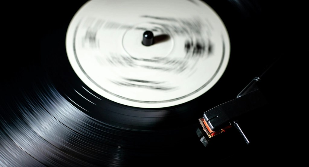 Close-up of a spinning vinyl record on a turntable, with a blurred white label and a stylus resting on the grooves.