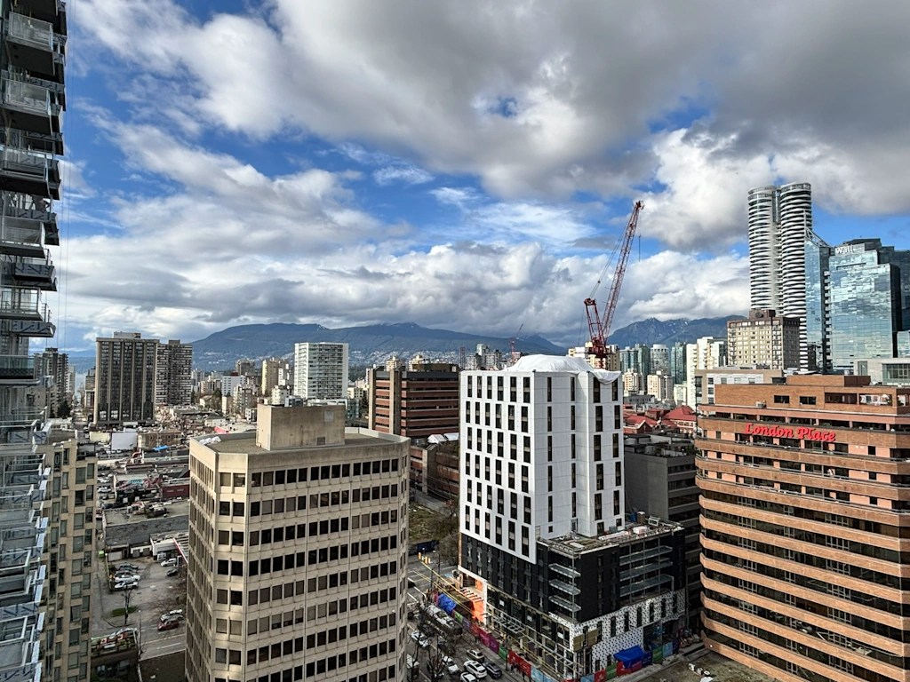 Urban skyline view of downtown Vancouver from a high vantage point, featuring mid‑rise and high‑rise buildings beneath a dramatic cloudy sky.