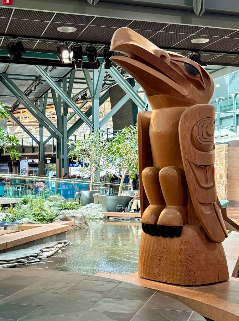 Large carved wooden eagle sculpture inside Vancouver International Airport, standing near an indoor water feature and surrounded by modern terminal architecture.